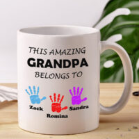 customized mug for grandpa, white ceramic mug displaying a text "This amazing granpa belongs to" and colourful handprints with names of grandchildren underneath each print