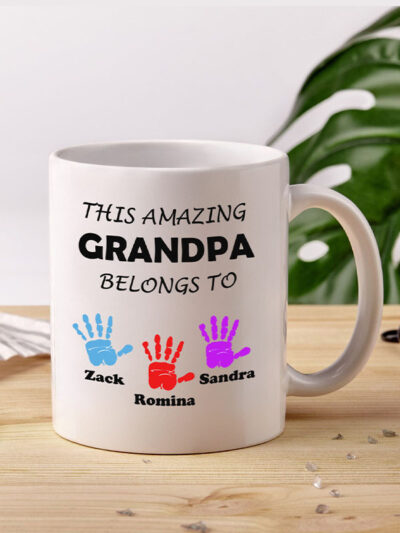 customized mug for grandpa, white ceramic mug displaying a text "This amazing granpa belongs to" and colourful handprints with names of grandchildren underneath each print
